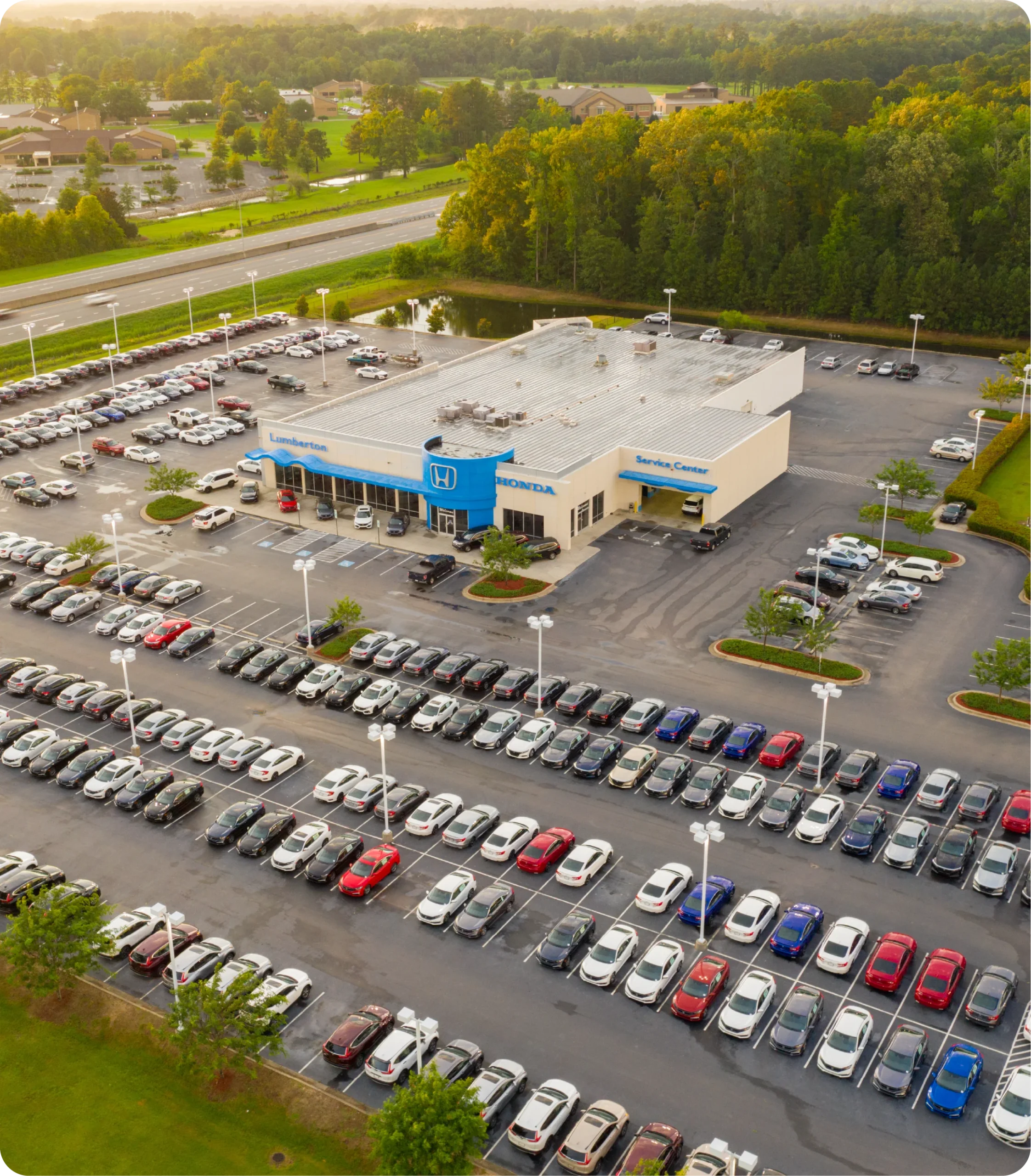 Vue aérienne d'un parking de concessionnaire automobile avec de nombreux véhicules garés et un bâtiment principal