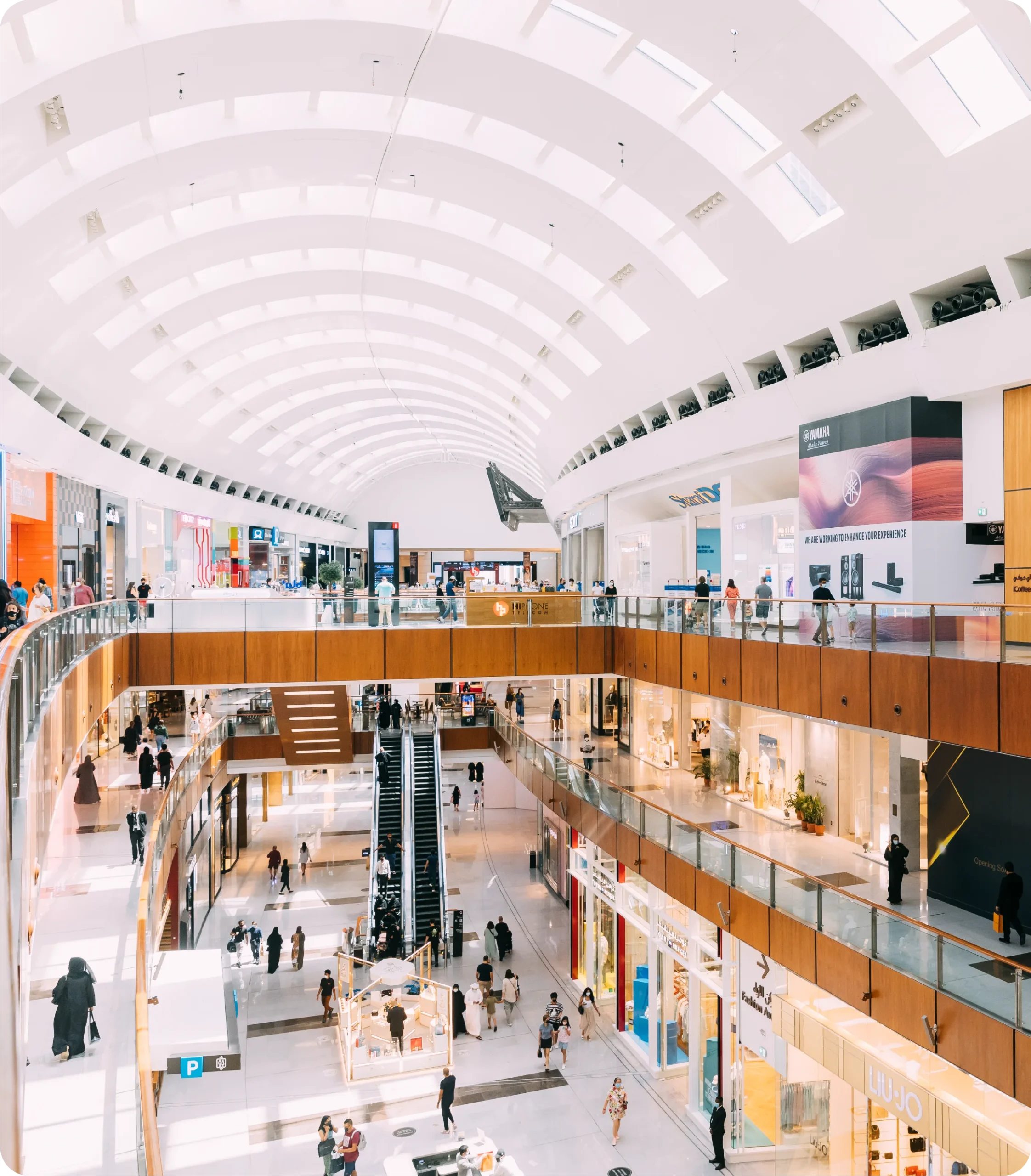 Vue intérieure d'un centre commercial moderne à plusieurs niveaux avec des escaliers roulants et des clients.