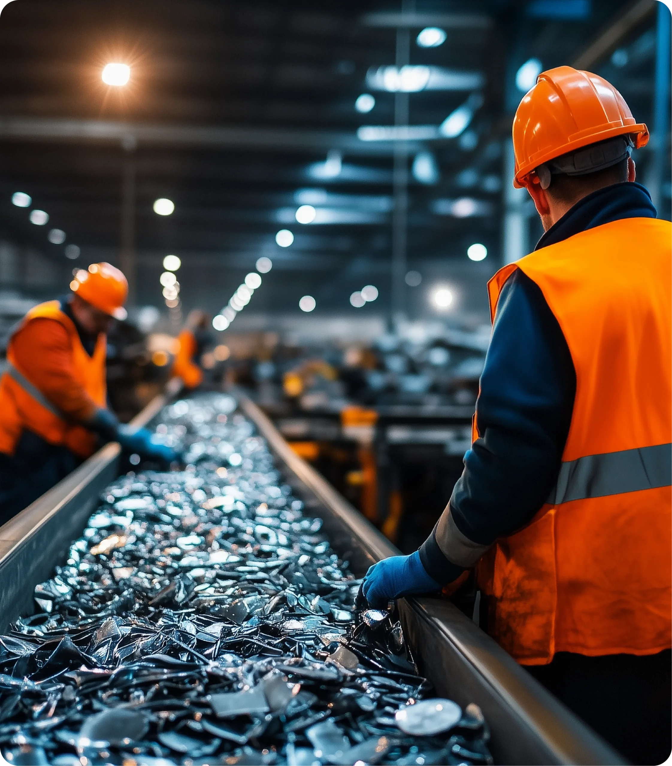 Des travailleurs en tenue de sécurité gèrent le traitement de la ferraille sur un convoyeur industriel.