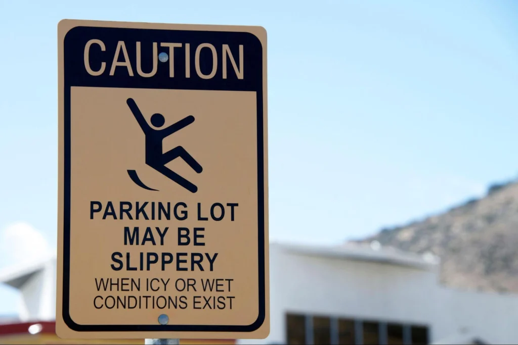Caution sign warning about slippery parking lots during icy or wet conditions for employee safety.