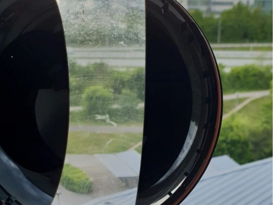 Couvercle de l'objectif d'une caméra de surveillance sale montrant une vue à moitié obstruée d'un paysage extérieur.