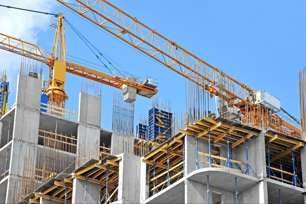 Chantier de construction de grande hauteur avec grues et structures en béton nécessitant une manutention sécurisée des matériaux