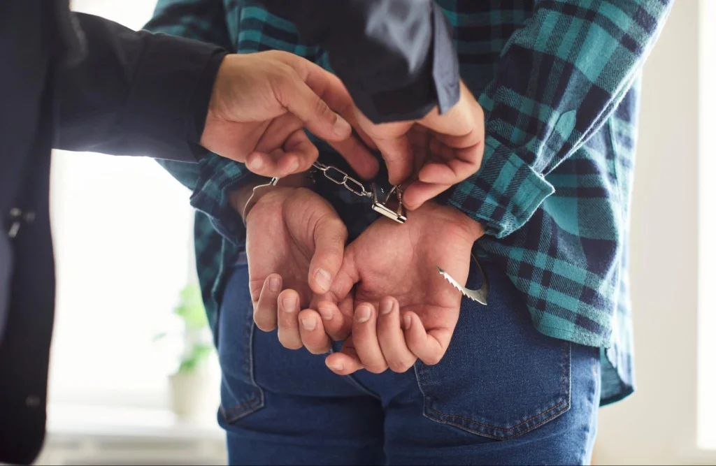 Policier menottant une personne vêtue d'une chemise à carreaux, symbolisant l'arrestation et l'action des forces de l'ordre.
