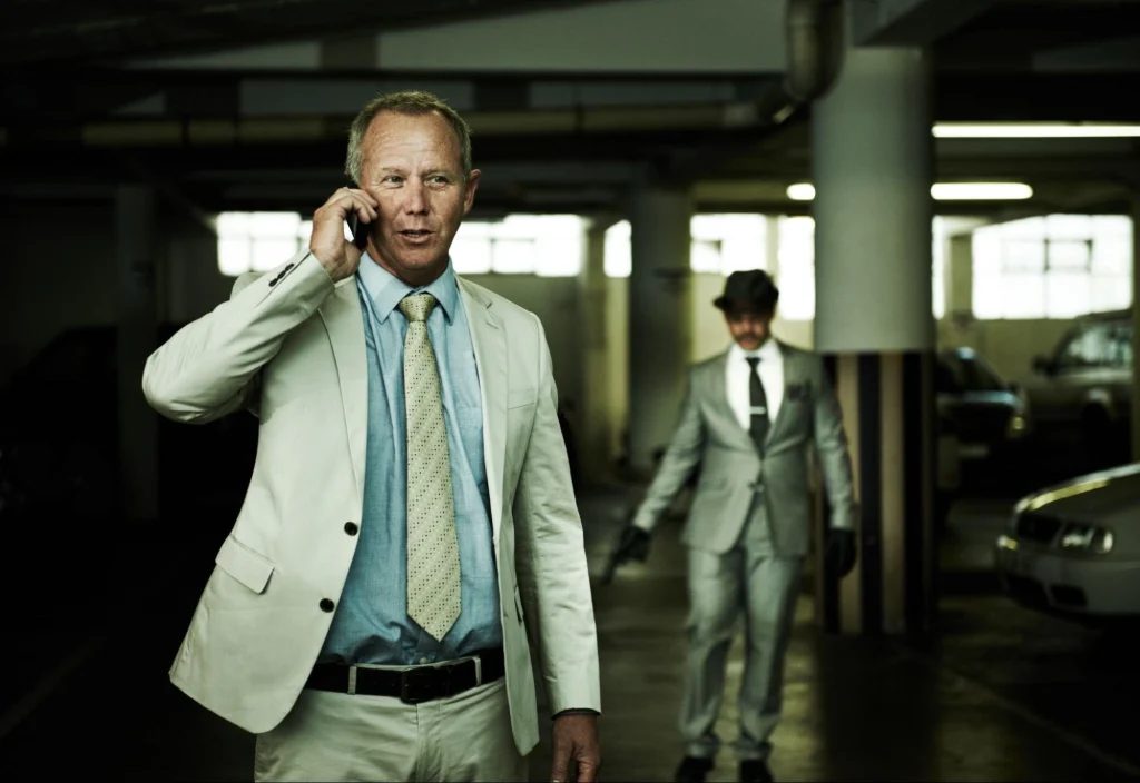 Two men in a parking garage, one talking on the phone while the other walks by, highlighting parking lot safety concerns.