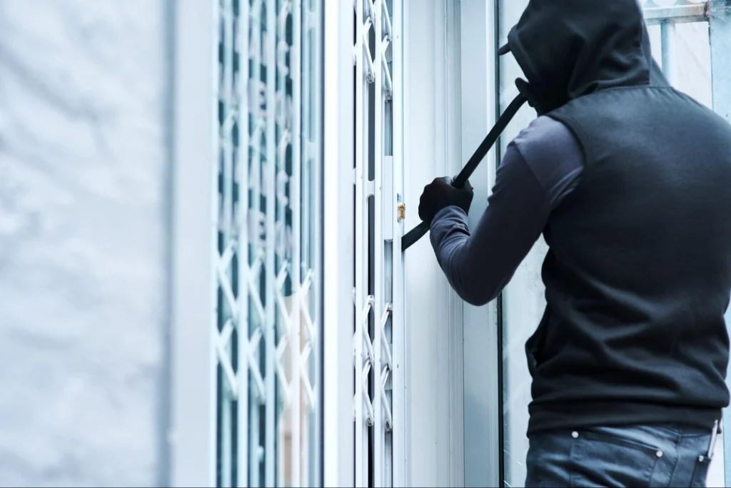 Masked burglar with crowbar attempting to break into property, symbolizing crime risks.
