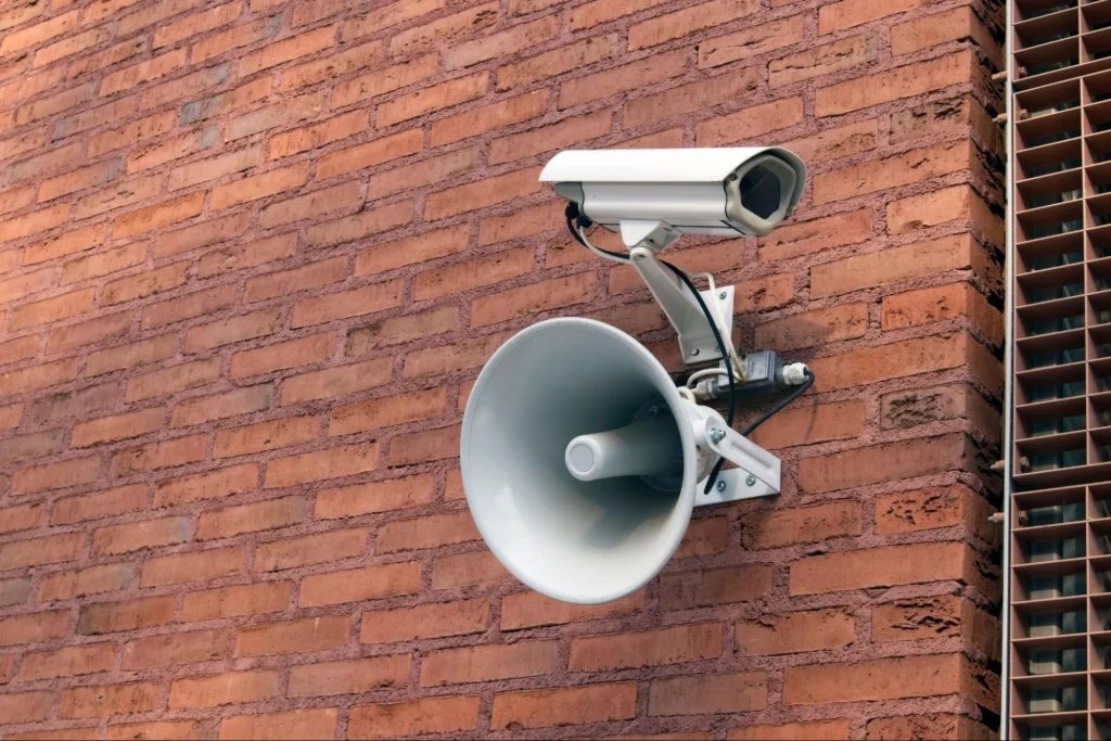 Caméra de sécurité et haut-parleur fixés sur un mur de briques à des fins de surveillance.